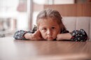 a sad little girl sits at a table with no food