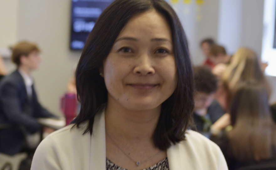 Woman stands in foreground with students at work in background.