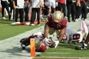 A football player dives over another as he reaches for the hash mark that denotes a touchdown.