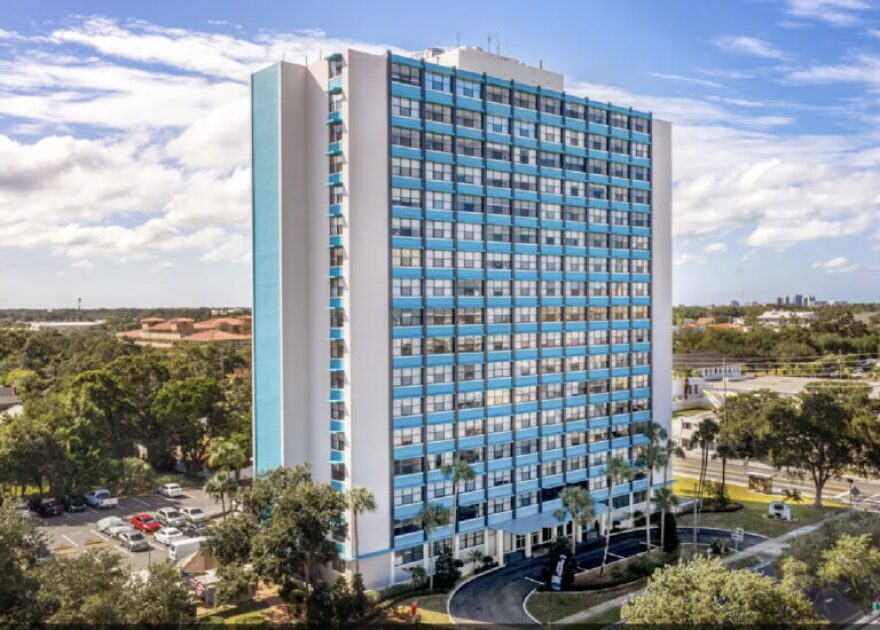A highrise blue and white building with trees surrounding it.