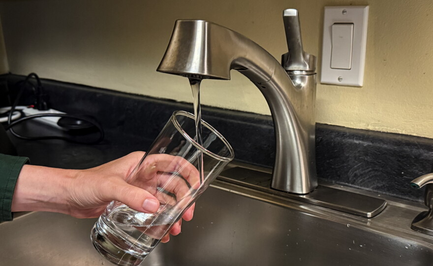 A hand holds a glass under a sink faucet as the glass fills with water.