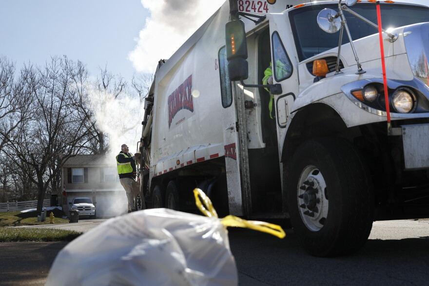 In this file photo, a sanitation worker rides the back of a truck as he works a residential route in Ohio.