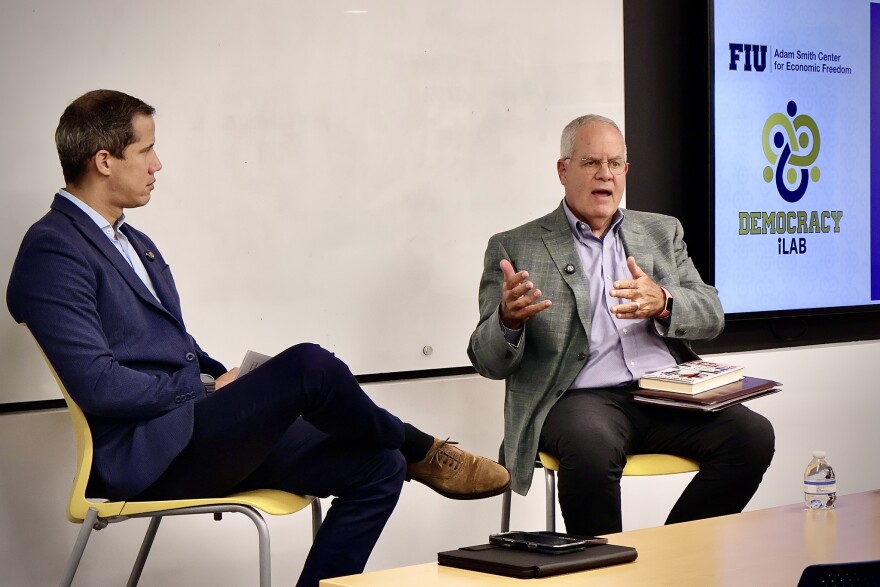  Both men are sitting on chairs engaged in discussion.