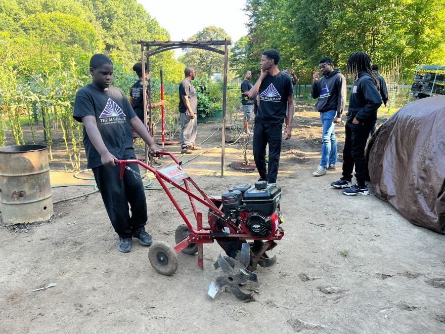 Victor Onipede, 12, drags a tiller from the shed to use in the garden.