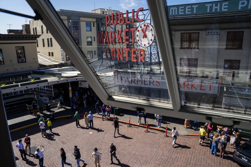 Pedestrians walk in the street at the corner of Pike Street and Pike Place at Pike Place Market on Fri., May 2, 2025. Pike Place Market is extending a pilot program to make the streets more pedestrian friendly by banning some cars from driving on the streets.