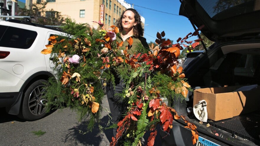 Laura Graham carries one of her pop-up flower installations to her car from the front of the Sun-Ray Cinema on Monday, Nov. 29, 2021.