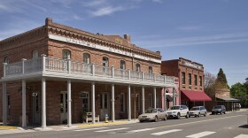 An old, brick building with a large wooden balcony along the entire second floor. A sign along the top says, "United States Hotel, Jacksonville, OR"