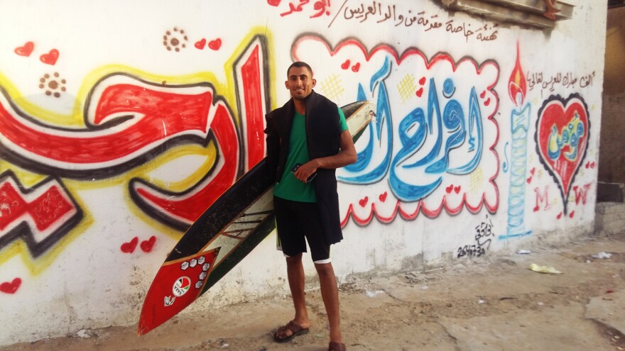 Ali Erheem, 25, poses next to graffiti on the front of his family's house in the Gaza Strip. Erheem is a member of the informal Gaza Surf Club. His painted his secondhand surfboard to look like a Palestinian flag.