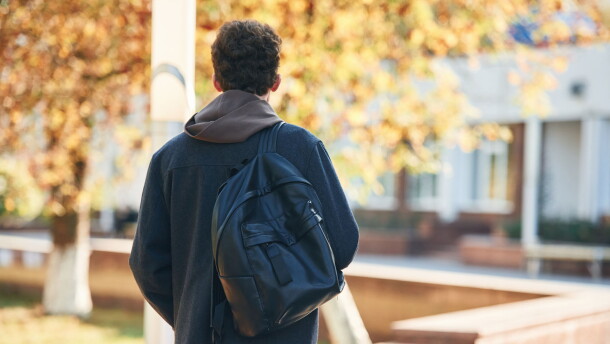 Back view. Young student is outside the university, in black clothes.