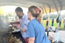 A woman in a blue shirt uses tongs to turn over grilling meat