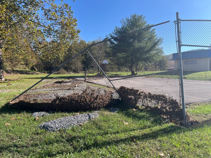 A chain length fence is bent in an area where a playground stood before Helene