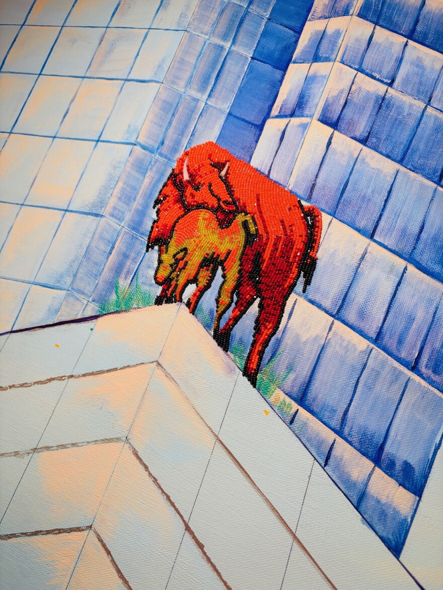 A close-up photo of a mama and baby bison, standing on the top of a corner of a tall painted building, with other large buildings behind them.