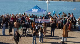 People gather for a group photo on a sunny day on the Santa Cruz Wharf with a banner that says "fight offshore drilling." 