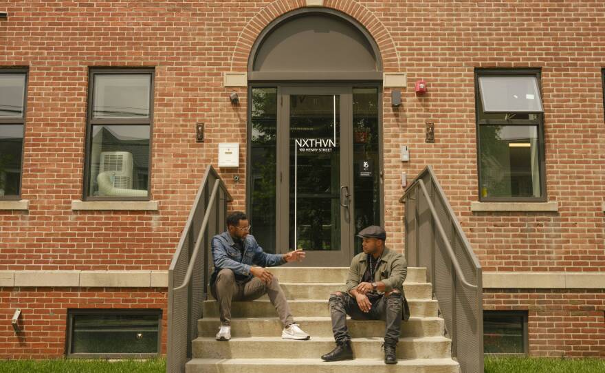 Jason Price and Titus Kaphpar sit talking on the steps in front of NXTHVN.