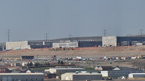 A sprawling set of warehouses top a denuded hill, with more buildings in the foreground.