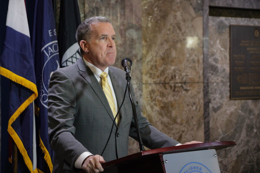 A man in a grey suit with a gold tie stands behind a podium.