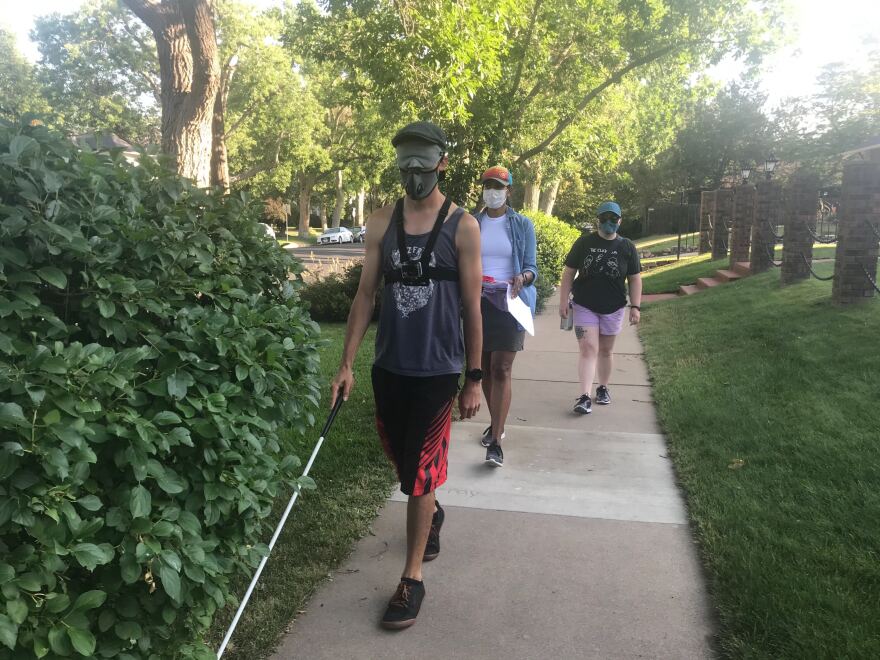 Kevin Cook in front, navigating a sidewalk with a white cane, followed by Silvia Correa-Torres and Rebekah Best