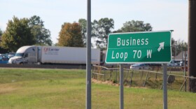 A green road sign that reads "Business Loop 70 W." A semi truck is parked in the background. 