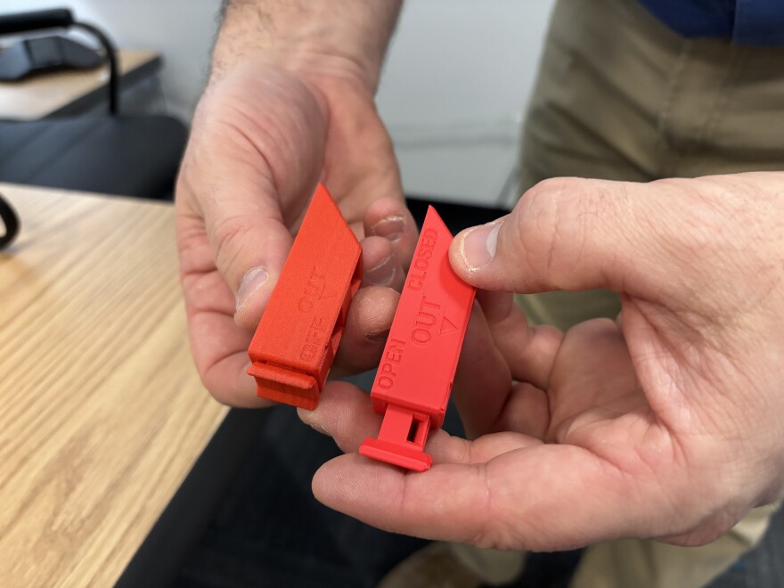 Robert Lewis, shift manager at Dominion Energy's Surry Power Station, holds two versions of a 3D printed circuit breaker locking device.