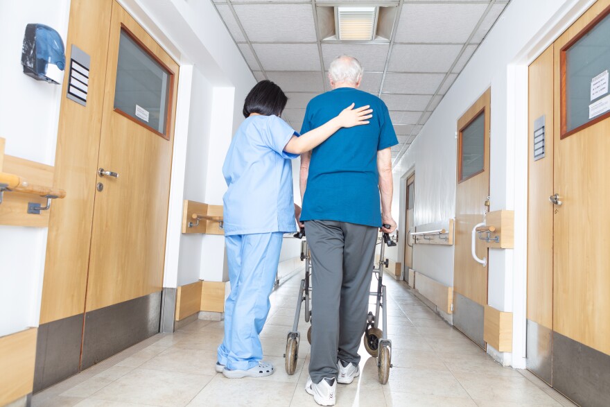 Asian nurse helping elder man walking in rehab facility.