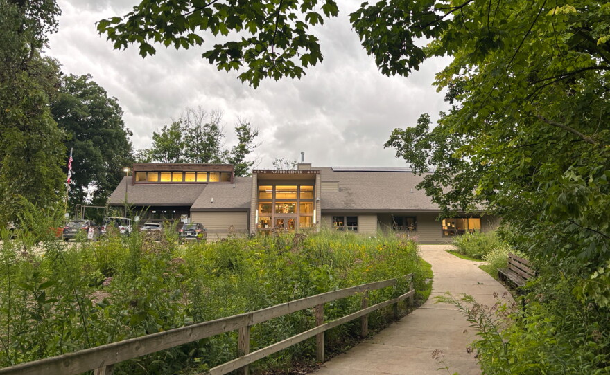A beige building with a glowing glass entry amongst trees.
