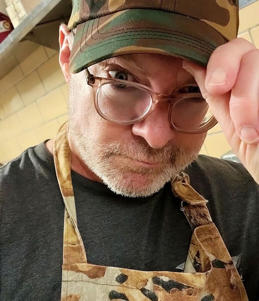 A man wearing an apron tips his cap.