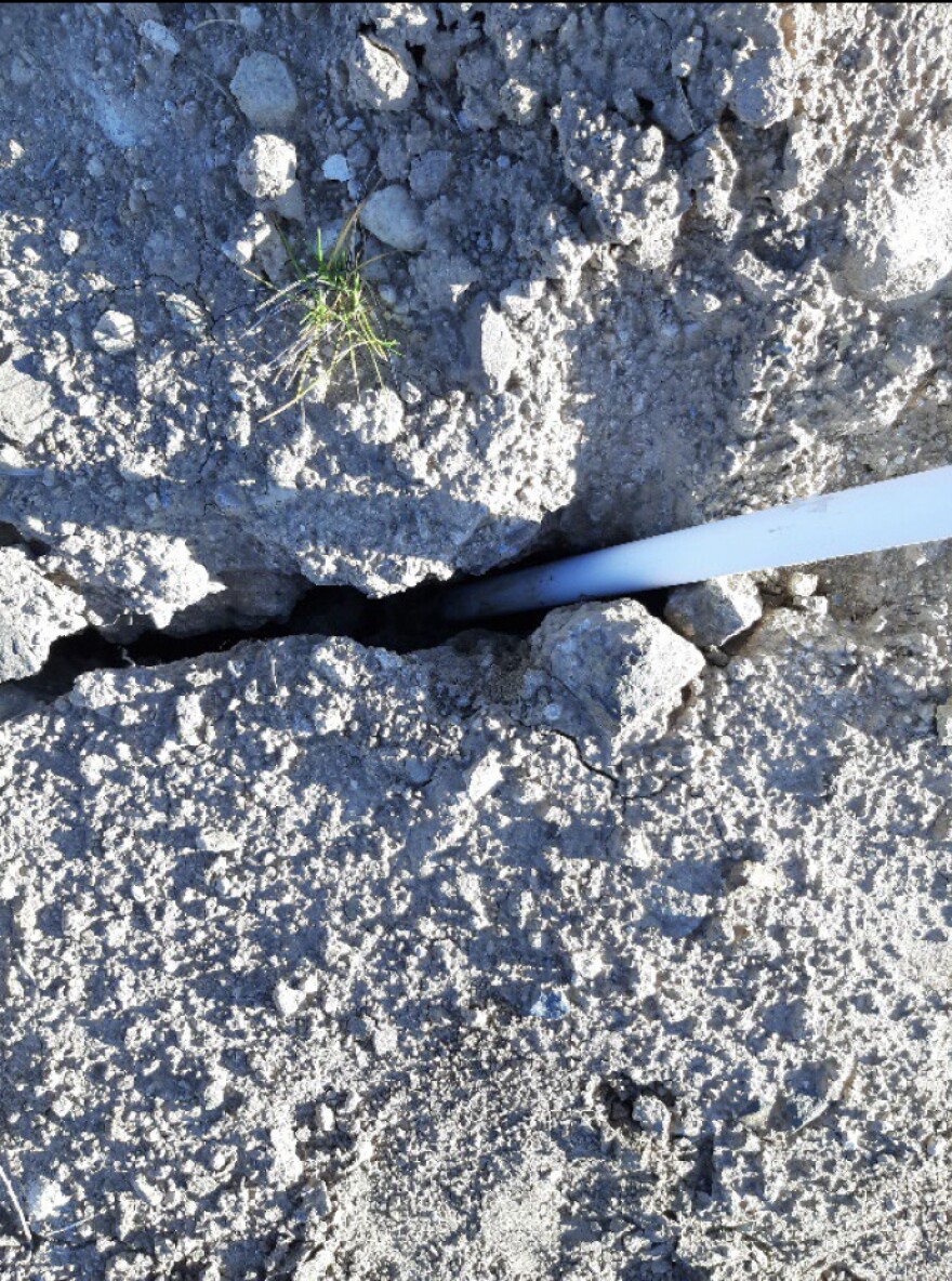 A white pole is stuck inside a crack in the ground.