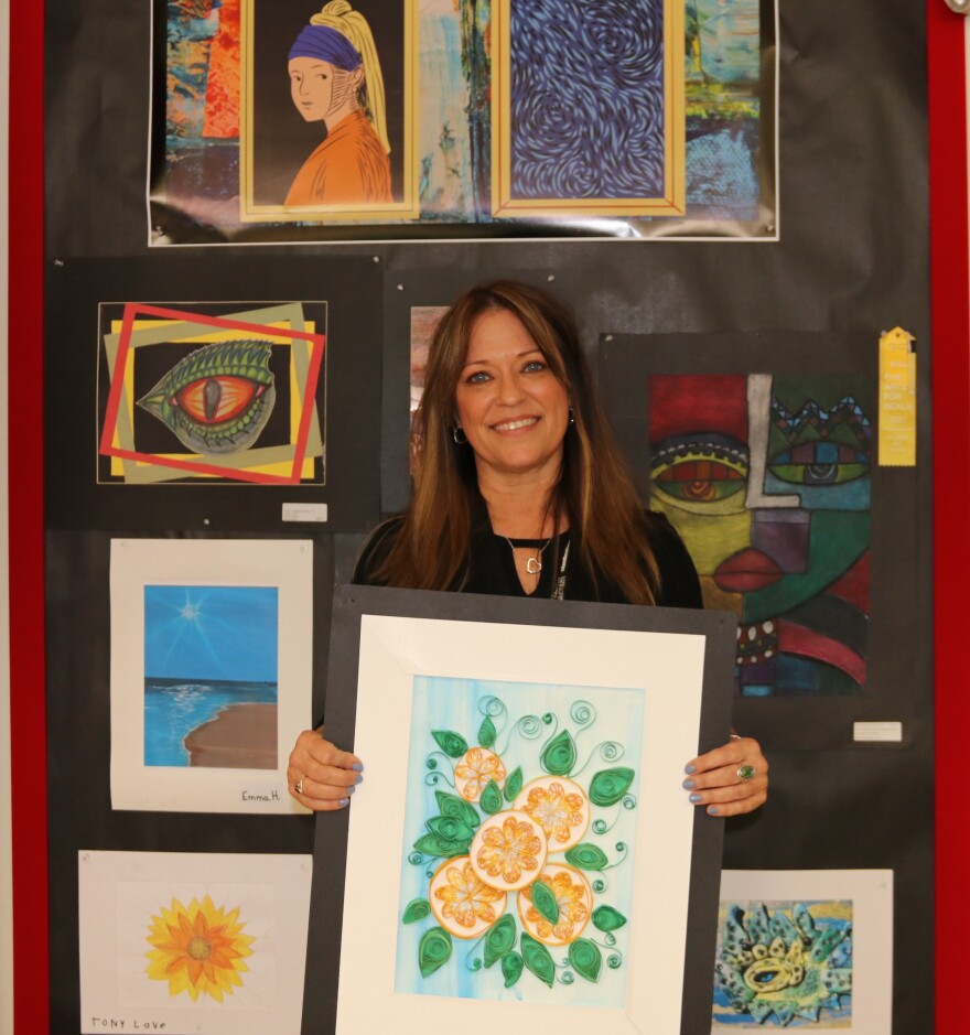 Hendry proudly holds up one of her students’ artworks on Tuesday, Feb. 17, 2026. “The most rewarding part of my day is when I see growth,” Hendry said. “They light up, especially when they’re so proud of their artwork, they’re so proud of the new technique they learned, or the new medium that they’re using.” (Amanda Roman/WUFT News)