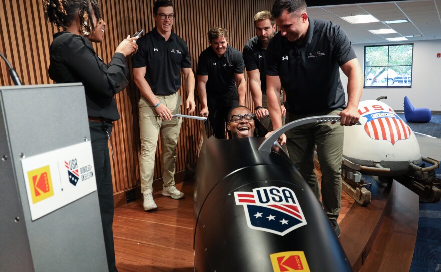 Hassan Williams climbs into the cockpit of the USA Olympic bobsled as Eastman Kodak Company announces its support of USA Bobsled/Skeleton ahead of the 2026 Winter Olympics, unveiling a new state-of-the-art sled in Kodak’s iconic yellow and red at the Golisano Institute for Business & Entrepreneurship. The historic 1956 Bronze Medal–winning “Tyler Sled,” designed and raced by Kodak engineers, was also on display.