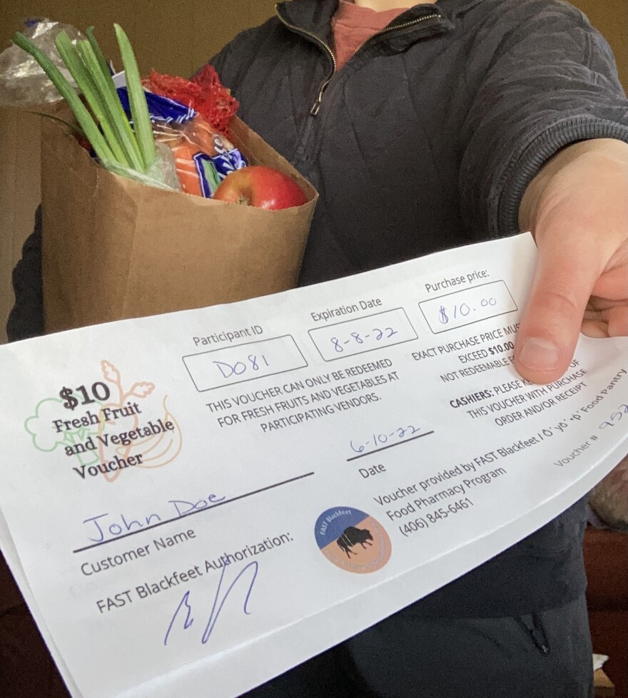 A hand holds out a voucher for $10 in fresh fruits and vegetables