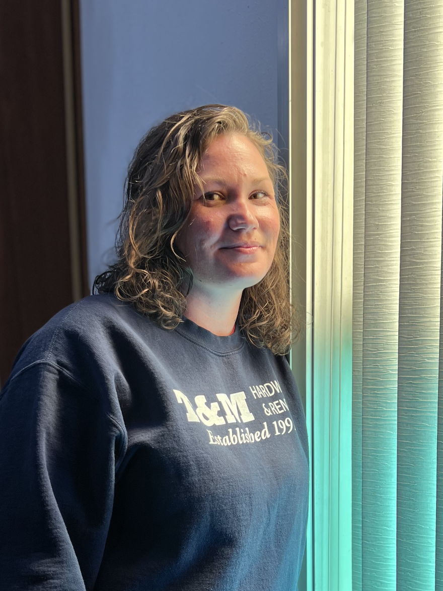 Amanda Hamrick stands beside blinds as colored light shines in.