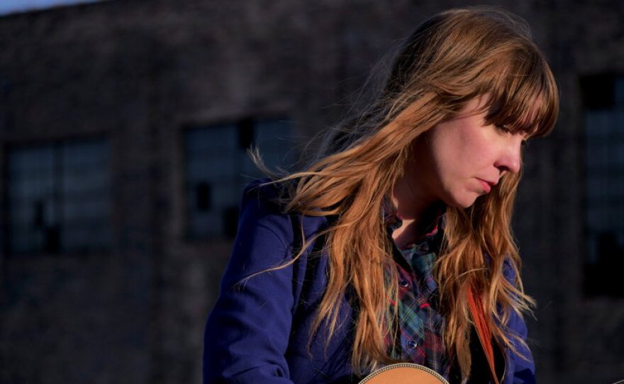 Folk artist Kelley Smith looks away while holding a guitar