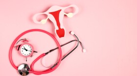 Women's health awareness concept. Uterus symbol with stethoscope and alarm clock on pink background. Copy space for text.