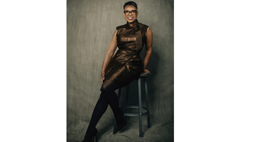 a woman poses in front of a camera sitting on a stool in a photography studio 