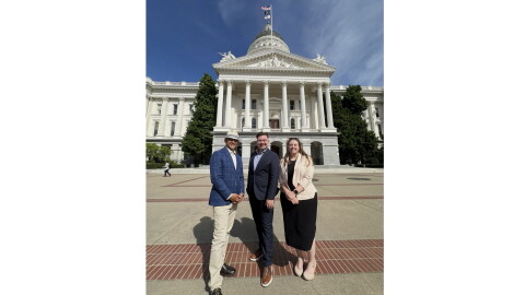 Three people stand in front of the California State Capitol on a sunny day. 