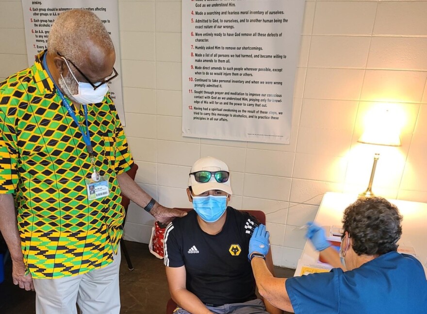 Dr. Washington Hill stands with his hand on a man's shoulder as he gets the COVID-19 vaccine