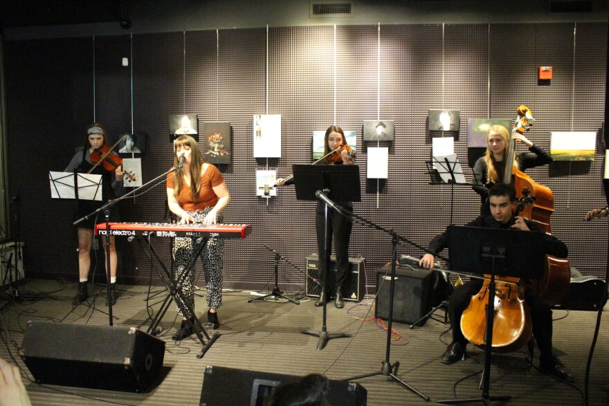 Woman standing playing a keyboard and singing with a string quintet behind her