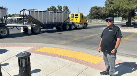 Firebaugh Mayor Freddy Valdez stands next to the intersection at Avenue 7 ½ and P Street in downtown Firebaugh on Aug. 26, 2026, as a farming truck crosses the intersection.