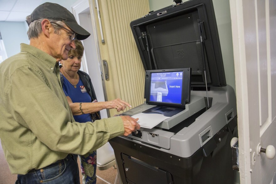 A man feeds a ballot into a voting machine with help from an election worker. 