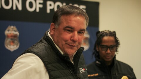 Columbus Mayor Andrew Ginther and Police Chief Elaine Bryant appear at a press event, in front of a backdrop decorated with police badges and the word "police." 