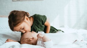adorable child kissing little sister lying on white bedding