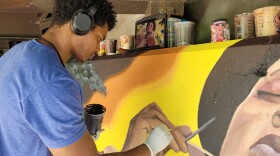 Waleed Johnson paints the hand of the main figure of his mural, a Black woman surrounded by light