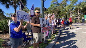 Demonstrators wave signs as people walked to Alico Arena to see and hear President Trump. Protestors shouted at Trump supporters, asking them about the Iran war, gas prices and the Jeffrey Epstein files.