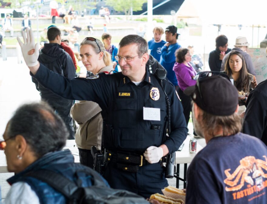 Former Juneau Chief of Police Bryce Johnson waves at a community barbecue it hosted in Marine Park to “be counted as a person against violence, against discrimination, and against hate” on July 20, 2016. (Annie Bartholomew/KTOO)