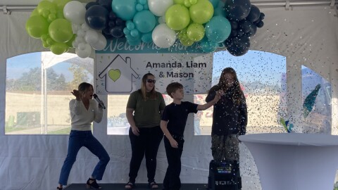Amanda Cole and her sons Liam and Mason pop a confetti filled balloon to find the keys to their new house, surrounded by Hayden Home employees and others who helped make their homeownership possible.
