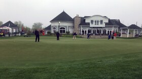 Golfers put on a practice green in front of a clubhouse building