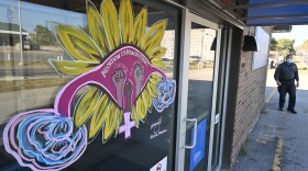 A man walks in the background at the Planned Parenthood Wyandotte County building where a large female reproductive organ, painted as a sunflower is colorfully displayed on the front plate-glass window of the brick building.