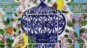 A series of painted tiles of three yellow birds around an ornate blue cage; additional ornamentation and designs of structures and plants frame the image