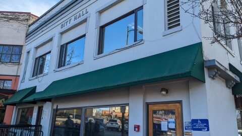 A two story grey build with large windows and green awnings. A sign at the top of the building says "City hall"