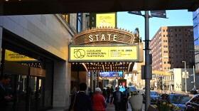 People walk down a sidewalk under a theater marquee sign